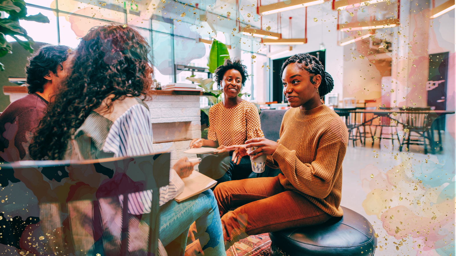 A group of four people sitting together in a modern, well-lit workspace, engaged in conversation. Two women in the foreground are smiling and holding notebooks and a cup, while the others listen attentively. The background features a casual, collaborative environment with plants, large windows, and artistic watercolor splashes with gold accents adding a creative and inviting touch.