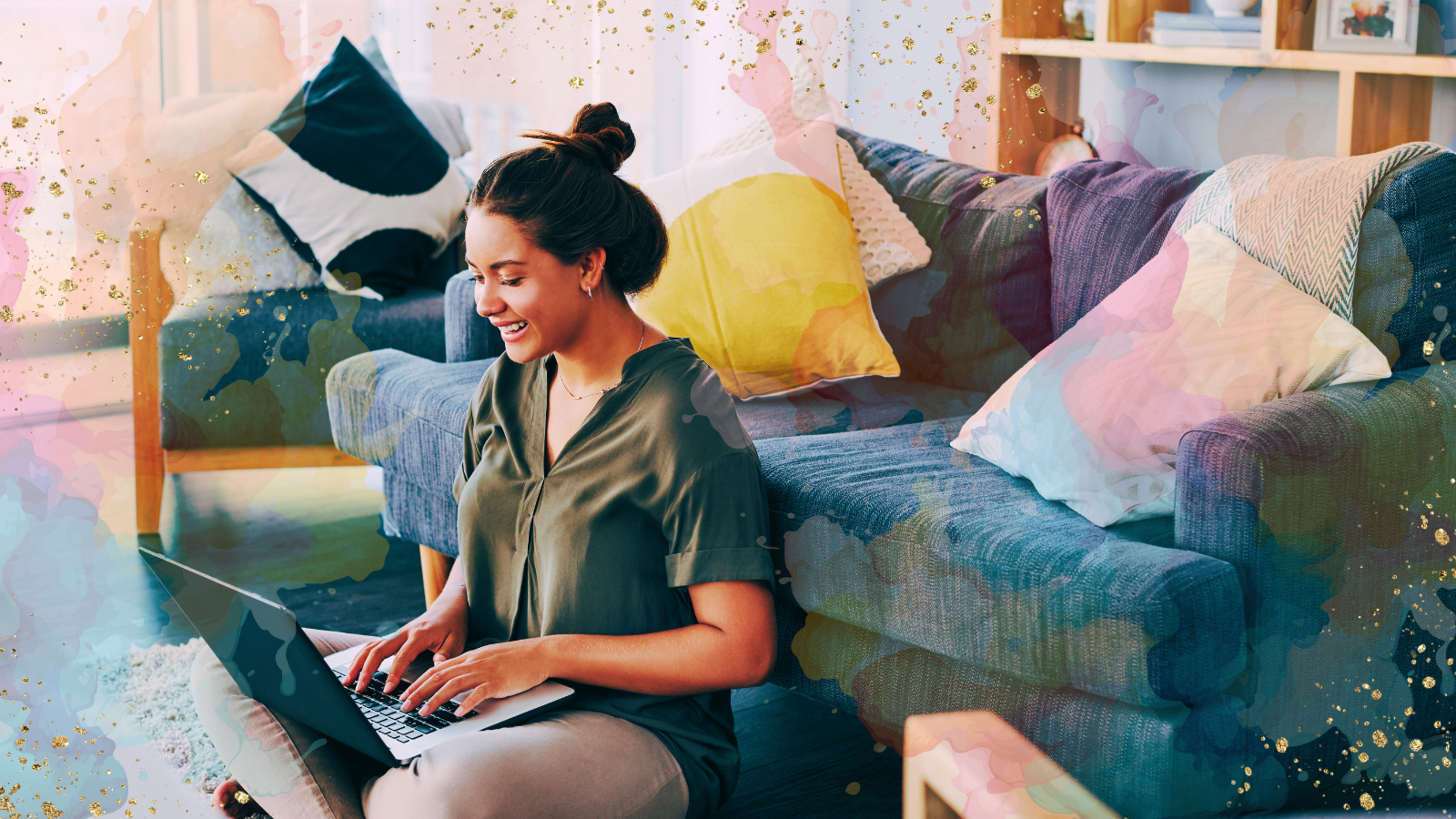 A woman sitting on the floor in front of a sofa, smiling while working on a laptop. The background features colorful watercolor splashes and golden accents, adding a creative and vibrant touch to the scene