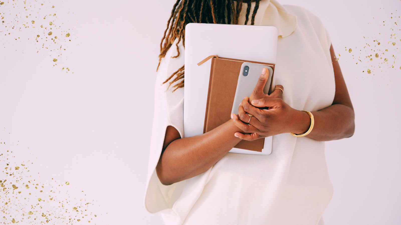 A close-up of a person holding a tablet, notebook, and smartphone against their chest. They are dressed in a white, sleeveless top, with gold jewelry adorning their wrist and fingers. Their hair is styled in long, natural locs, and the background is a soft pastel pink with golden sparkles scattered throughout, adding a touch of elegance to the composition.