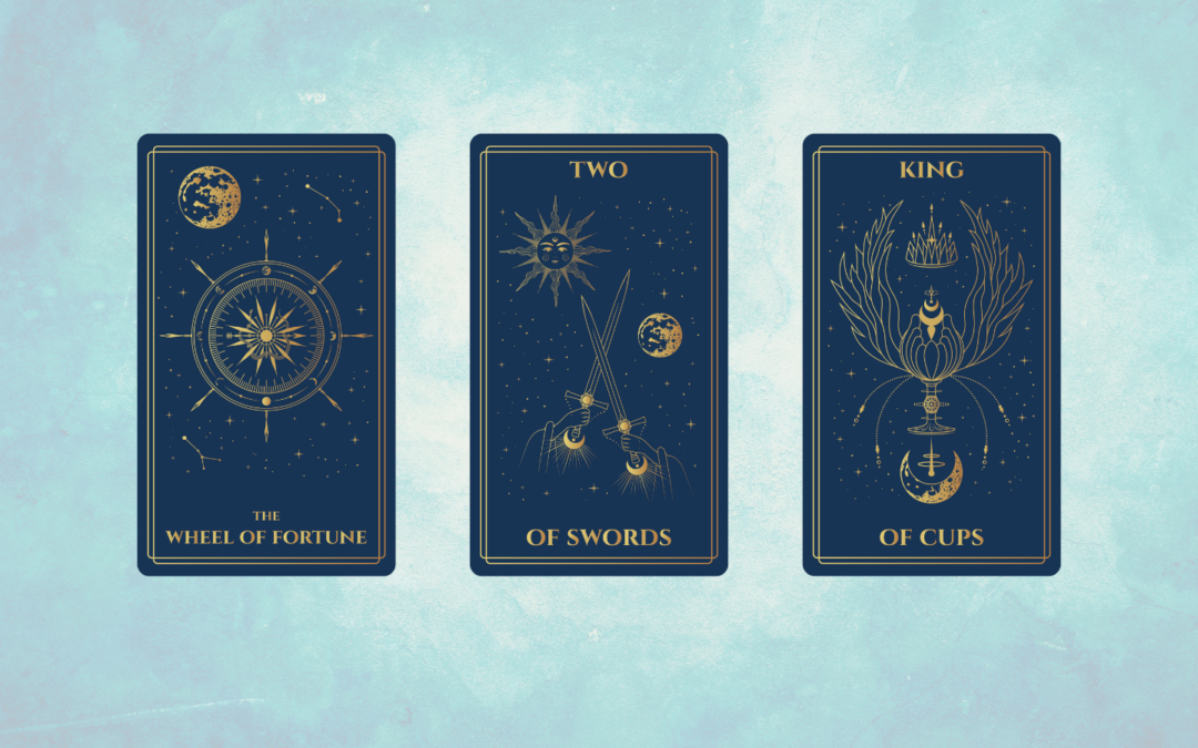 A digital tarot spread set against a soft blue background displays three elegant, dark blue cards with gold illustrations. From left to right: The Wheel of Fortune shows a celestial compass surrounded by stars and a golden moon; the Two of Swords features two crossed swords beneath a starry sky with a moon and sun above; and the King of Cups depicts a crowned, abstract cup with wing-like shapes and lunar symbols beneath a canopy of stars.