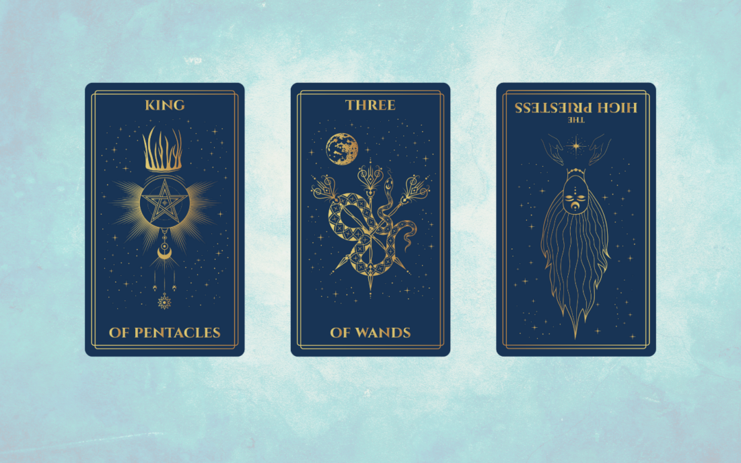 A digital tarot spread displayed on a soft blue background shows three dark blue cards with gold illustrations. From left to right: the King of Pentacles features a crowned pentacle with radiating lines and celestial symbols; the Three of Wands shows a geometric, intertwined serpent and wands beneath a full moon; and the High Priestess reversed depicts an upside-down crowned figure with flowing hair and a star held between two hands above.